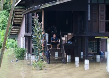 SEORANG penduduk termenung di atas tangga rumahnya yang dinaiki air di Kampung Padang Luar, Jitra, Kubang Pasu. - UTUSAN/ SHAHIR NOORDIN