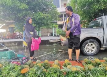 SALLEH Mat Isa menjual nanas kepada pelanggan di petak perniagaannya dalam keadaan air pasang besar di Teluk Intan, semalam. – UTUSAN/AIN SAFRE BIDIN