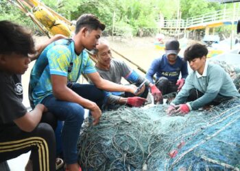 ZAKARIA Ibrahim (tiga dari kiri) bersama beberapa rakan nelayan membersihkan pukat selepas pulang dari laut di Kampung Pulau Ketam, Kuala Perlis, Perlis, semalam. - UTUSAN/IZLIZAN OTHMAN