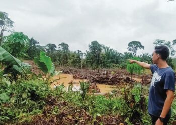 MUHAMMAD Fazli Omar menunjukkan paras sungai dibelakang rumahnya di Kampung Naram, Slim River, Tanjung Malim yang tidak surut sejak Ahad lalu. – UTUSAN/MEGAT LUTFI MEGAT RAHIM