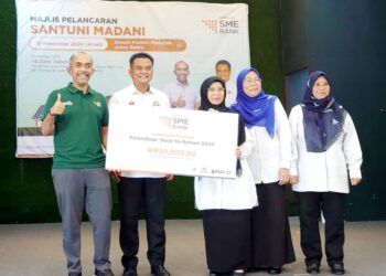 ZAHARI Sarip (dua dari kiri) menyampaikan replika cek berjumlah RM20,000 sumbangan SME Bank kepada 14 buah sekolah pada Majlis Pelancaran Santuni Madani di Kampung Pasir, Johor Bahru.