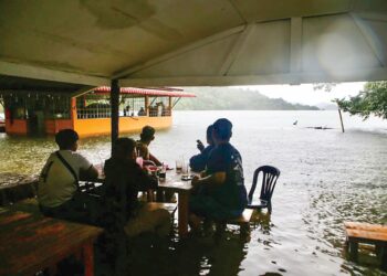PELANGGAN menikmati makanan berasaskan ikan air tawar di sebuah kedai yang dilimpahi air ekoran hujan berpanjangan di Tasik Gubir, Sik. – UTUSAN/SHAHIR NOORDIN