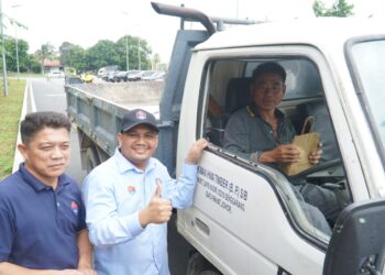 MOHAMAD FAZLI Mohamad Salleh (tengah) menyampaikan bungkusan kepada pengguna jalan yang melalui Jalan Kampung Rahmat merentasi estet Sri Gading, Batu Pahat.