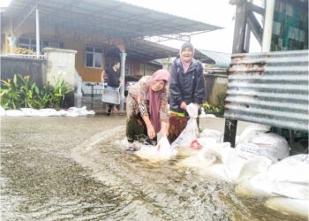 WAN Som Wan Dollah (kiri) bersama Pah Mat Ali membina benteng guni pasir bagi menghalang arus deras merosakkan rumah mereka di Kampung Dalam Rhu, Tumpat, Kelantan. – UTUSAN/ROHANA ISMAIL