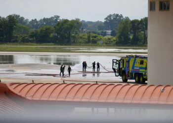 SEBAHAGIAN kakitangan dan anggota bomba lapangan terbang membersihkan landasan terbang LTSAH yang dinaiki air dalam kejadian banjir di Alor Setar. - UTUSAN/ SHAHIR NOORDIN