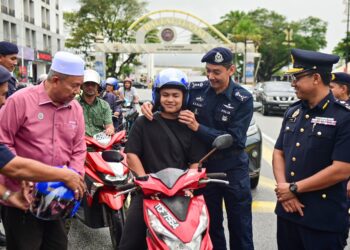 MALIAMAN Kassim (kiri) diiringi Mohd. Zamri Samion (kanan) dan Mohd. Khairi Khairudin (dua dari kanan) mengagihkan topi keledar percuma kepada penunggang motosikal semasa program Kempen Keselamatan Jalan Raya sempena Musim Perayaan Tahun Baru Cina di Kuala Terengganu, hari ini. - UTUSAN/PUQTRA HAIRRY