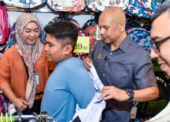 ARMIZAN Mohd. Ali (dua, kanan) membantu salah seorang penerima memilih baju seragam sekolah sempena PJRM Kembali Ke Sekolah di Pusat Beli-belah ITCC Penampang, Sabah, hari ini.