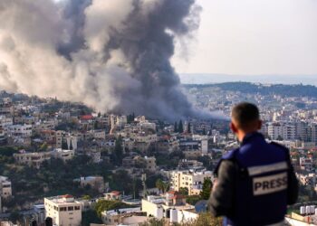 SEORANG wartawan melihat kepulan asap dari tapak serbuan Israel di kem pelarian Jenin di Tebing Barat.-AFP
