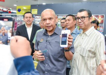 ARMIZAN Mohd. Ali (tengah) menunjukkan penggunaan terminal MyKad dalam membeli barang keperluan asas di sebuah pasar raya di ITCC Penampang semalam