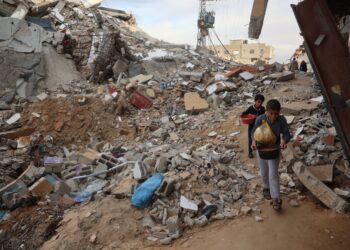 KANAK-KANAK Palestin membawa bungkusan makanan sambil melalui celah runtuhan bangunan di tengah Semenanjung Gaza, kelmarin. - AFP