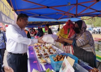KHALID Mohamed (kiri) menyerahkan beg kempen kepada seorang peniaga di Bazar Ramadan MITC, Ayer Keroh, Melaka. - UTUSAN/MUHAMMAD SHAHIZAM TAZALI
