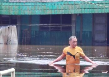 SUPERYADI Zainal mengharungi air ‘banjir termenung’ ketika meninjau keadaan rumahnya di Kampung Seri Gambut, Pekan Nanas, Pontian.