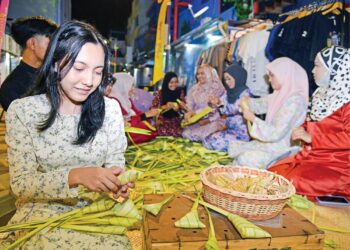 CHAVALIN Prichacon Somphon bersama anak-anak muda yang lain menganyam ketupat di pasar lokal nostalgia raya di Kangar Street Art, pekan lama Kangar, Perlis semalam. – UTUSAN/IZLIZAN OTHMAN