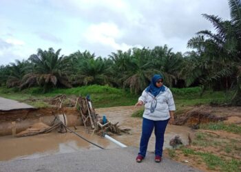 FAUZIAH Misri melihat keadaan jalan utama di Felcra Sungai Layau, Kota Tinggi yang runtuh susulan hujan lebat empat hari lalu.