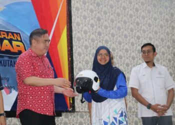 LOKE Siew Fook (kiri) menyampaikan topi keledar piawaian SIRIM kepada penerima pada program pertukaran topi keledar bersama penduduk di Jerantut, Pahang. - UTUSAN/SALEHUDIN MAT RASAD