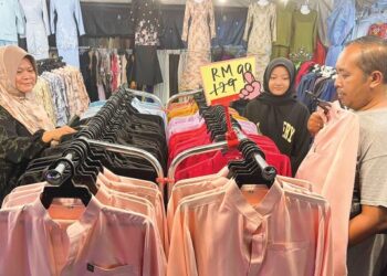 SEORANG peniaga melayan salah seorang pelanggan yang sedang memilih baju Melayu yang diturunkan harga selepas jualan masih perlahan di bazar Aidilfitri Sena, Kangar, Perlis semalam. – UTUSAN/IZLIZAN OTHMAN