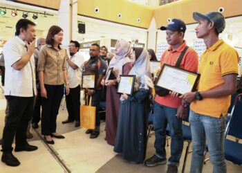 (Dari kiri) Mohd. Azmi Mohd. Lila  dan Sandrea Ng Shy Ching menyantuni penerima surat tawaran RMR di Ipoh, Perak hari ini. - UTUSAN