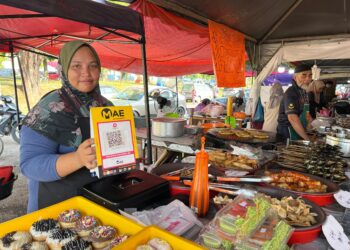 WAN Norainun Wan Rozelan menunjukkan salinan kod QR yang disediakan kepada pelanggan di Bazar Ramadan Kompleks Perdana Majlis Daerah Gua Musang (MDGM) di Gua Musang, Kelantan. - UTUSAN/AIMUNI TUAN LAH