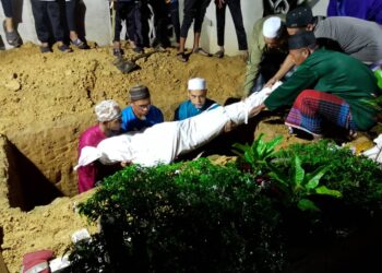 JENAZAH Halim Mat Razi dibawa masuk ke dalam liang lahad untuk dikebumikan di Tanah Perkuburan Islam Nibong, Padang Kala, Peringat, Kota Bharu, Kelantan malam tadi.-UTUSAN/ROHANA MOHD. NAWI.