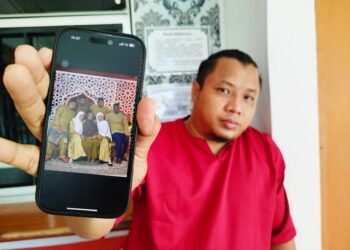 RIFAAI Adzraai menunjukkan gambar raya keluarga yang diambil di studio baru-baru ini dengan arwah adiknya paling kanan sekali. - UTUSAN/FADZIL ZAINOL