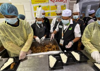 MOHD. HISHAM Harun (kanan) melihat proses pembungkusan makanan untuk diedarkan kepada jemaah haji Malaysia di Dapur Al Wafa, Mekah baru-baru ini.