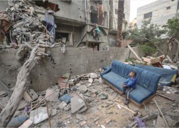 SEORANG kanak-kanak duduk di atas sofa yang rosak sambil memerhatikan orang ramai membersihkan runtuhan dari sebuah rumah di kem pelarian Nuseirat di tengah Semenanjung Gaza. – AFP