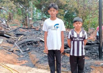 MUHAMMAD Asyraf Haris Maznizan (kiri) bersama Muhammad Farish Rayyan di hadapan rumah yang terbakar di Kampung Mogol, Ulu Tembeling di Jerantut, Pahang. – UTUSAN/HARIS FADILAH AHMAD