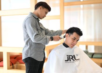 MUHAMMAD Musyrif Amni Mohd. Nizam sedang memotong rambut pelanggan di kedainya di Kangar, Perlis.