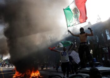PENUNJUK perasaan memegang bendera Mexico sambil berdiri di atas kereta semasa protes terhadap serbuan imigresen di Los Angeles, California, kelmarin.- AFP