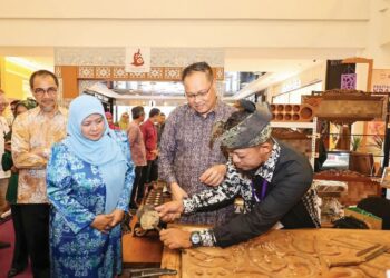 MOHD Yusri ( kanan) dan ‘Ainu Sham( kiri) melihat produk kraf ukiran kayu yang ditempah oleh pembeli ketika sesi Walkabout FKPT 2025 di East Coast Mall, kelmarin.