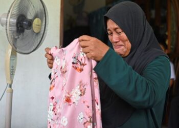 Norinda Kasim melihat blaus anaknya, Nur Dalila Farhana yang dihantar bersama barangan lain anaknya oleh UPSI di Kampung Baru Tok Dor, semalam. – UTUSAN/PUQTRA HAIRRY