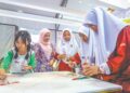 LOI Yi Jing (kiri) dan Nur Zazatul Ain Annura Mohd Fadzil (tiga dari kanan) sedang merasai pengalaman mewarna batik di reruai MOTAC yang menjadi tarikan golongan belia.