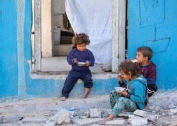 KANAK-kanak Palestin duduk berhampiran pintu rumah yang rosak sambil menjamah makanan di Bandar Gaza.- AFP