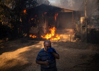 SEORANG lelaki berdiri di hadapan sebuah rumah yang dijilat api dalam kebakaran hutan di Pikermi di timur Athens, Greece.-AFP