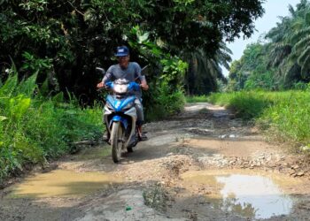 PENDUDUK menunjukkan keadaan jalan yang rosak di Kampung Batu Hitam, Pasir Salak, Perak. – UTUSAN/AIN SAFRE BIDIN
