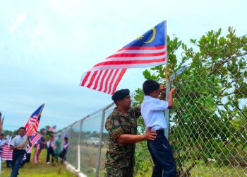 SEORANG anggota tentera membantu pelajar memasang bendera di salah sebuaj sekolah di Pulau Banggi, Kudat, Sabah baru-baru ini.