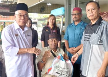 HASSAN Abdul Karim (kiri) menyampaikan sumbangan barangan keperluan kepada beberapa asnaf di Kampung Bendahara, Johor Bahru hari ini.-UTUSAN