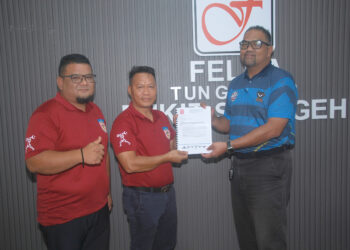 Ahmad Janius Abdullah (tengah) menyerahkan dokumen permohonan penajaan kepada Faireez Zulkifli 
di pejabat Felda Tun Ghafar Bukit Senggeh, Nyalas, Jasin, Melaka.