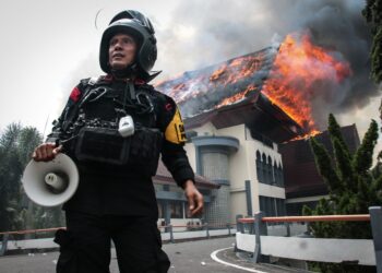 SEORANG anggota polis berdiri sambil memegang pembesar suara ketika bangunan pejabat Majlis Perwakilan Rakyat Daerah Wilayah Nusa Tenggara Barat dibakar oleh penunjuk perasaan di Mataram, Pulau Lombok, Nusa Tenggara Barat.-AFP