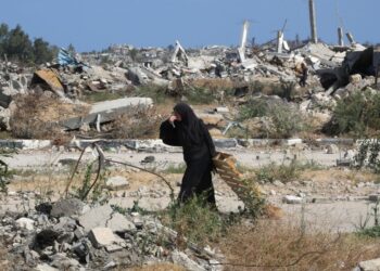 SEORANG wanita Palestin berjalan sambil membawa sekeping kayu di kawasan yang musnah akibat serangan Israel di tengah Gaza.- AFP
