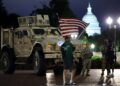 SEORANG penunjuk perasaan mengibarkan bendera kebangsaan AS terbalik ketika anggota Pengawal Kebangsaan berkawal di sebelah kenderaan perisai di luar Stesen Union, Washington, kelmarin.- AFP