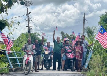 Pramoot Puan (tengah, baju hijau) bersama komuniti Siam memasang Jalur Gemilang di Kampung Padang Petani, Kangar, Perlis, semalam.