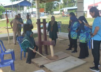 NORAZIAH Kassim (duduk) sedang menunjukkan proses padi ditumbuk di dalam lesung indik sebelum menjadi emping. – UTUSAN/HARIS FADILAH AHMAD