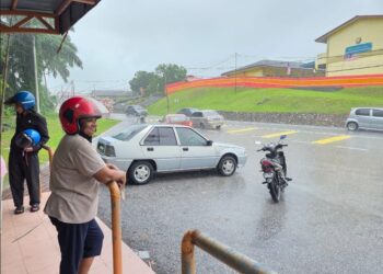 SEORANG wanita berteduh di tempat menunggu bas ketika hujan lebat Sungkai dekat Tanjung Malim, Perak semalam. - UTUSAN/AIN SAFRE BIDIN
