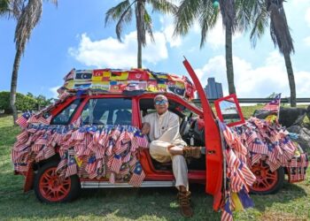 AZMI Mansor bersama Proton Tiara miliknya yang penuh dihiasi Jalur Gemilang dan bendera negeri-negeri ketika ditemui di tepi Lebuhraya Persekutuan, Petaling Jaya, Selangor. –  UTUSAN/SYAKIR RADIN
