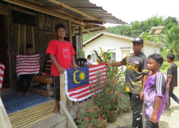 JUMAAT Arom (dua dari kanan) bergotong-royong memasang Jalur Gemilang di rumahnya di Kampung Redip, Pos Hau, Gua Musang, Kelantan. – UTUSAN/AIMUNI TUAN LAH