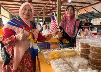 HAFIDZAH Mustakim (kiri) memasang Jalur Gemilang di Pasar Kubang Pasu Kota Bharu, Kelantan. - UTUSAN/ ROSLIZA MOHAMED