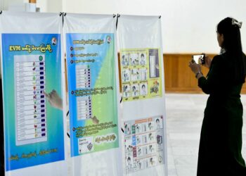 SEORANG wanita merakam gambar poster panduan pengundian semasa sidang media pertama UEC Myanmar di Naypyidaw.-AFP