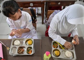 MURID di sebuah sekolah rendah di Jakarta sedang menikmati hidangan yang disediakan menerusi program makanan percuma kerajaan.- AFP