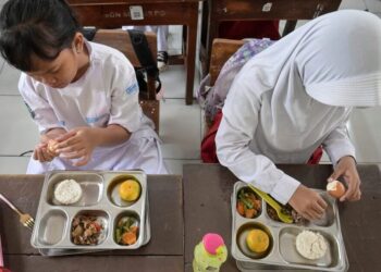 MURID di sebuah sekolah rendah di Jakarta sedang menikmati hidangan yang disediakan menerusi program makanan percuma kerajaan.- AFP